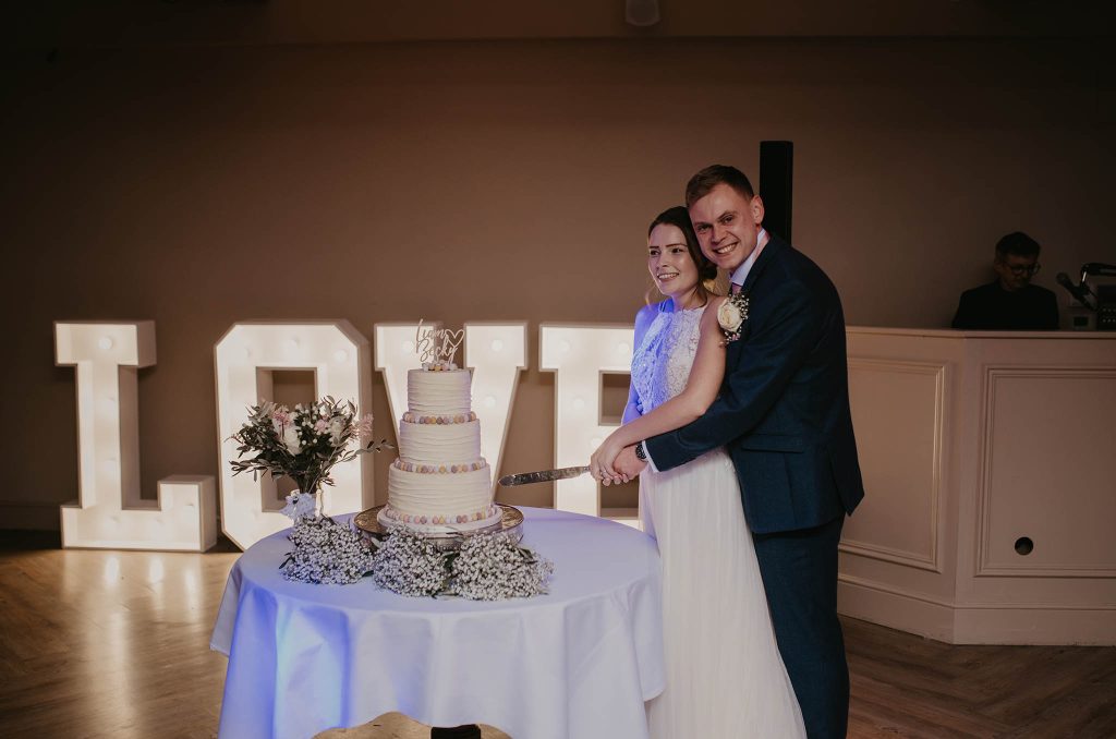 bride and groom cutting their cake decorated with mini eggs - by nikki terra who loves photographing quirky wedding details in Hampshire