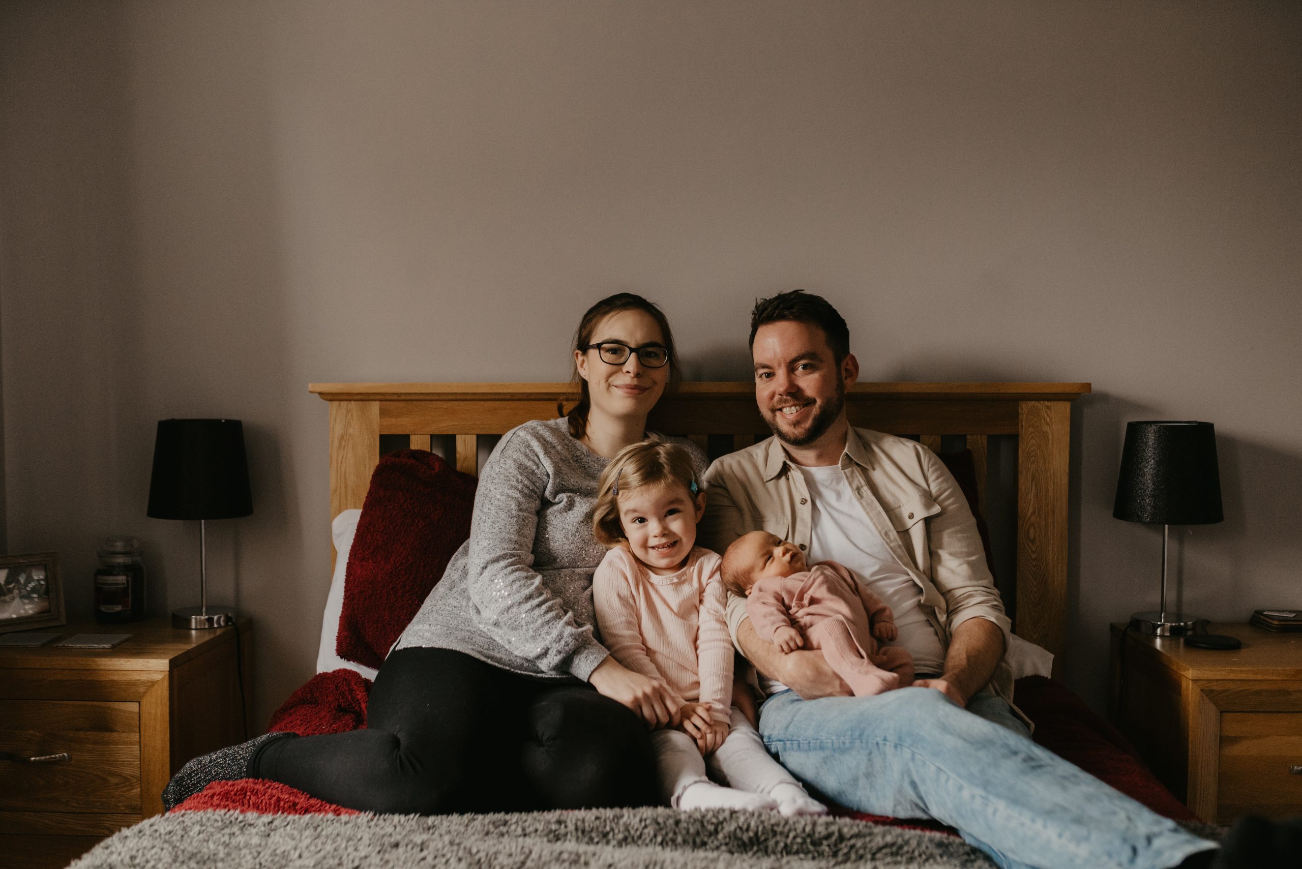 family with parents and two children on their bed, by in-home newborn photographer in Hampshire 